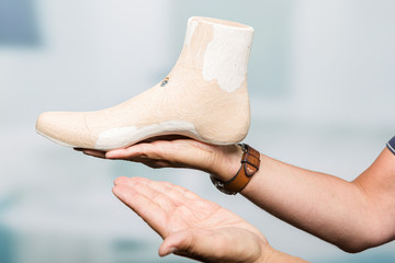 hands of a orthopedic shoemaker presenting an individual crafted wooden last