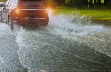 Spraying water of a car moving driving car on flooded road during flood caused by torrential rains....