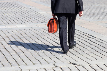 Man in a business suit carrying leather briefcase walking on the street, back view. Concept of...