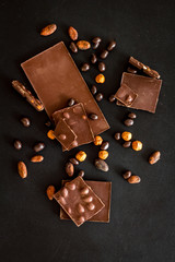 Chocolate with nuts and its ingredients on black background top view