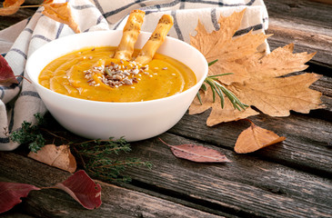 Pumpkin cream soup with seeds, rosemary, thyme, spices and autumn leaves on a wooden background. Thanksgiving food.