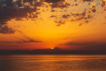 Sea landscape with sunrise, mountains and cloudy sky