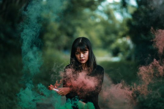 Portrait of Asian woman in black cloth with color fire smoke in forest witch concept