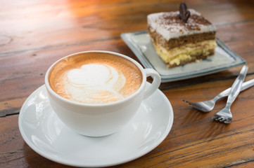 Hot coffee cup on plate with tiramisu cake.