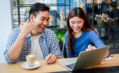 Asian couple in blue shirt drinking coffee talking and working with computer laptop smile and  happy mood in coffee shop cafe