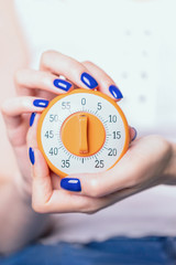 Female hands with blue manicure holding kitchen timer on a light background. Time control concept