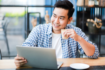 Asian man using laptop and drinking coffee in coffee shop cafe working online freelance business