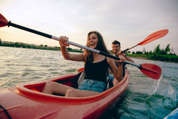 Confident young caucasian couple kayaking on river together with sunset in the backgrounds. Having...