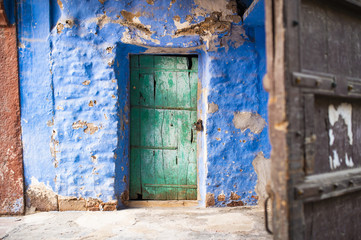 Close-up view of an old blue house with a green wooden door in Jodhpur, Rajasthan, India. Jodhpur is the second-largest city in the Indian state of Rajasthan, India.