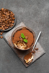 Portion of Classic tiramisu dessert in a glass cup on dark concrete background