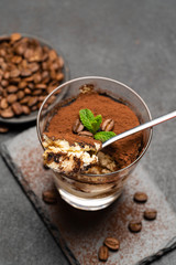 Portion of Classic tiramisu dessert in a glass cup on dark concrete background