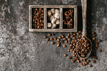 Coffee beans in wooden spoon on dark textured background.