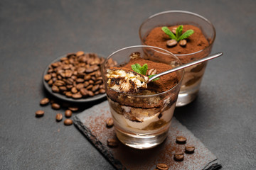 Portion of Classic tiramisu dessert in a glass cup on dark concrete background