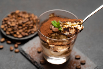Portion of Classic tiramisu dessert in a glass cup on dark concrete background