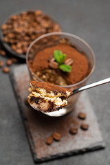 Portion of Classic tiramisu dessert in a glass cup on dark concrete background