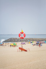 View of a beach with lifeguard lookout post, with lifebuoy and surfboard. Beach with people...