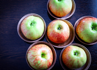 Six fresh apples in paper plates on a brown table, top view