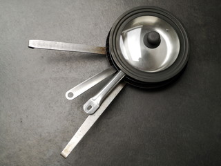 Pfannen mit Griff aus Edelstahl mit Deckel auf grauem Betonboden in einer Designerwohnung im...