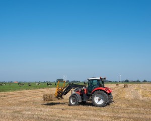 farmer with tractor collects straw bales on sunny summer day in dutch province of groningen
