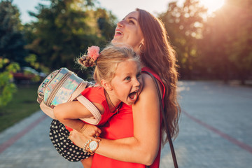 Happy mother meeting her daughter after classes outdoors primary school and tickling kid. Family...