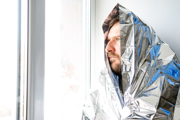a man with a beard is wrapped in a large shiny material and looks out the window