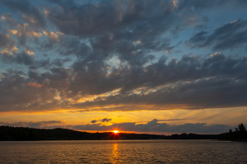 Amazing sunset in Finland during summer evening. Golden hour and dramatic clouds. Reflection in water, calm scenery.