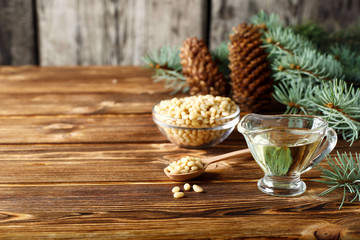 Cedar products: cedar oil, nuts, cones, brunches on a wooden broun background.