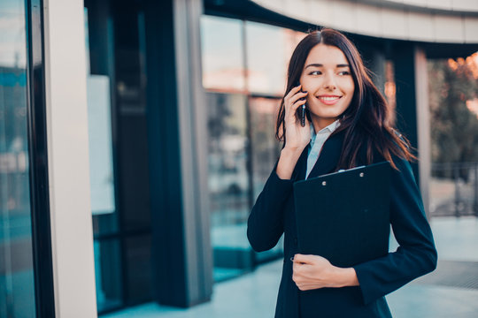Successful smiling businesswoman or entrepreneur talking to the phone standing in front of his office.
