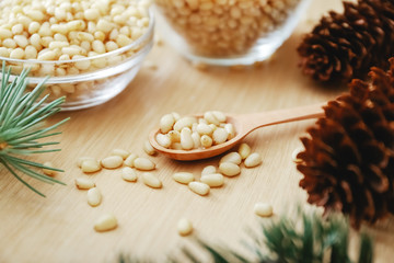 Pine nuts on a wooden spoon with cedar branches, cones on a beige background.