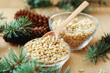 Cedar pine nuts in glass bowls with cones, spoon, cedar brunch on wooden background.