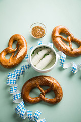 Münchener Weißwurst in Terrine und Brezel mit Oktoberfest Luftschlangen auf Pastell grünen Hintergrund