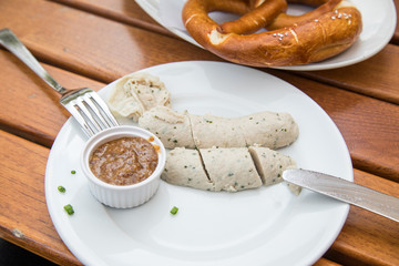 Münchener Weißwurst ohne Pelle mit Messer und Gabel, süßen Senf und Brezel draußen in Biergraten