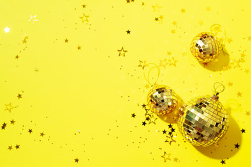 Creative Christmas concept. Shiny gold disco balls over yellow background. Flat lay, top view. New year baubles, star sparkles. Party time. Greeting card