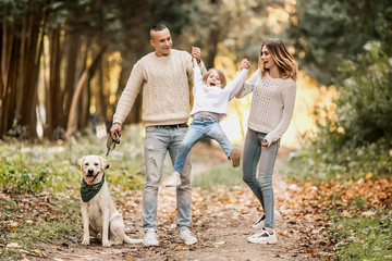 Happy beautiful family with dog labrador is having fun together walking the in park.