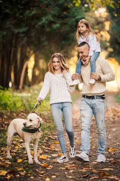 Happy beautiful family with dog labrador is having fun together walking the in park.