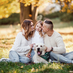 Fototapeta premium Happy beautiful family with dog labrador is having fun are sitting on green grass in park.