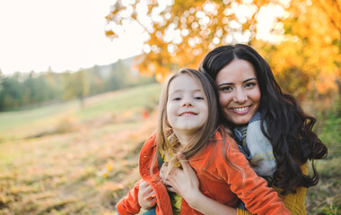 A portrait of young mother with a small daughter in autumn nature at sunset.
