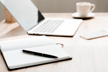 selective focus of notebook with pen near gadgets on table