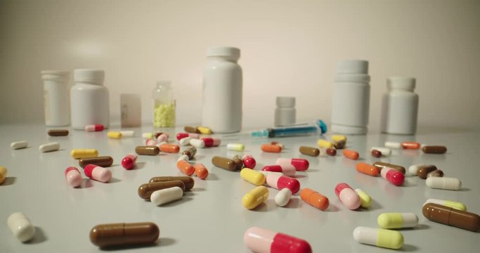 A range of pills, tablets cans and syringes on white table, representing modern addiction to drugs and medicine - pharmaceutical industry concept 4k footage