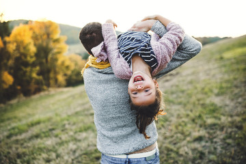 A rear view of young father having fun with a small daughter in autumn nature.