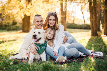 Obraz premium Happy beautiful family with dog labrador is having fun are sitting on green grass in park.