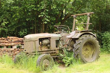 Obraz premium old and rusty tractor surrounded by grass and trees