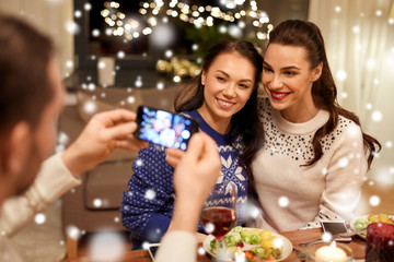 holidays and celebration concept - happy friends having christmas dinner at home and taking picture by smartphone over snow