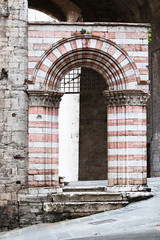 Photograph of an ancient door with columns and arch, in the center of Perugia, made of white and pink bricks.