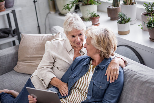 Mature lesbian couple looking at digital tablet together on sofa