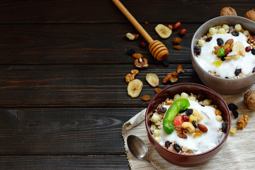 Granola with yougurt, nuts, dried fruits on wooden brown background