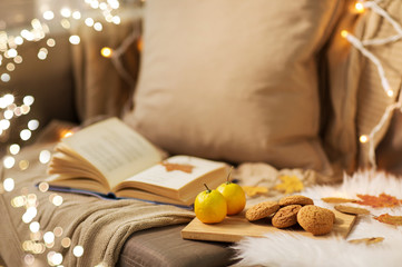 Naklejka na ściany i meble hygge and cozy home concept - lemons, book, almond nuts and oatmeal cookies on sofa