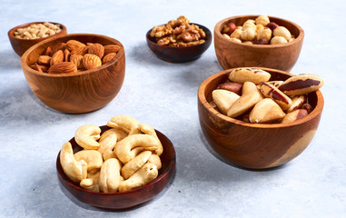 Obraz na płótnie Canvas pecans, hazelnuts, almonds, pine nuts, cashews in wooden bowls on blue background