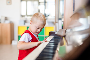 A down-syndrome school boy sitting at school, playing piano.