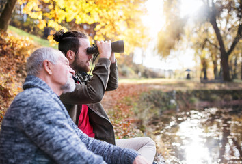 Senior father and his son with binoculars in nature, talking.